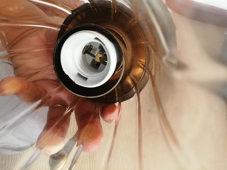 Closeup details of E27 socket on brown tint glass lamp with polished metal plates and rings ornament.